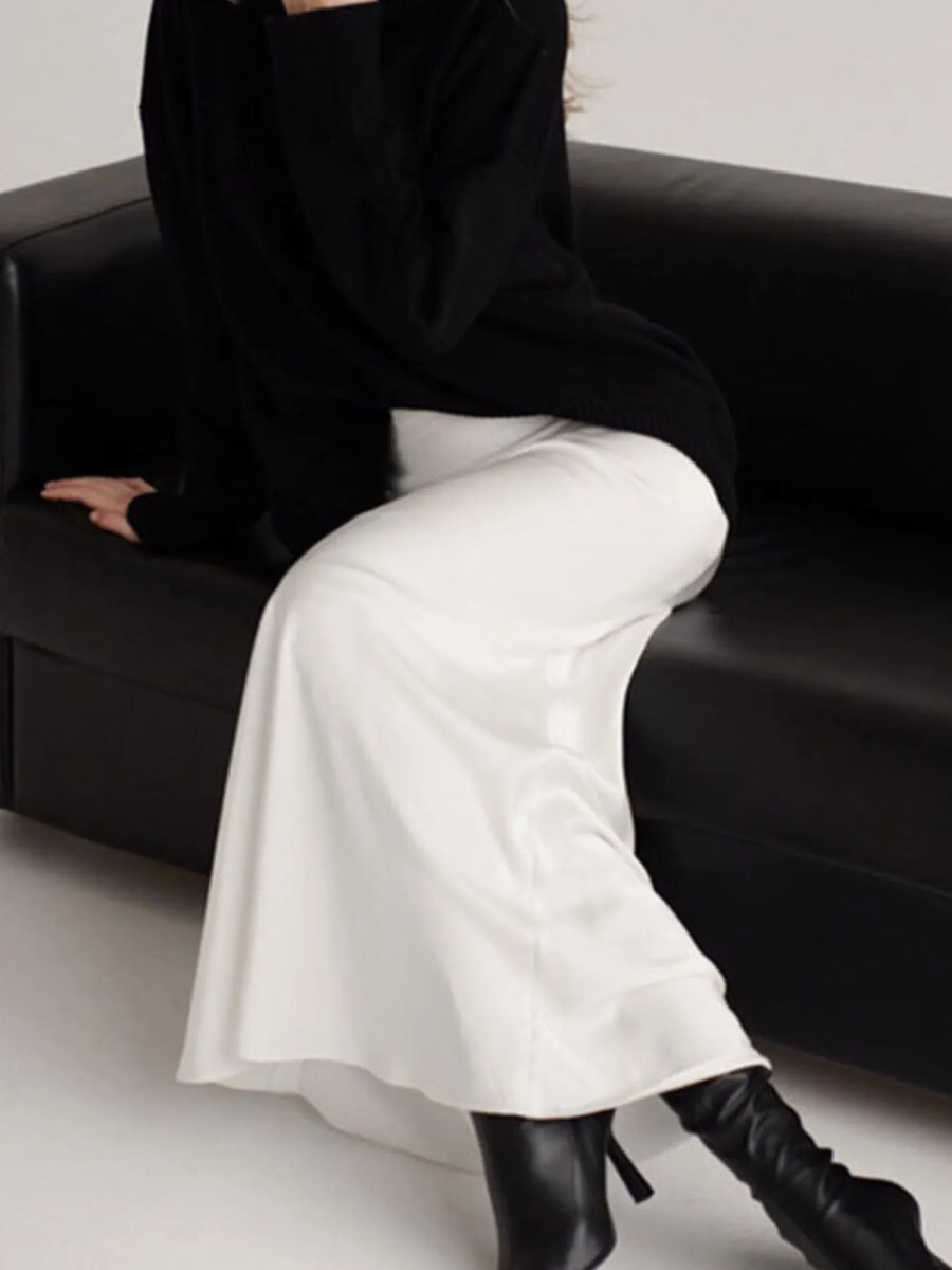 Person wearing a black outfit with white pants and black boots sitting on a black couch.