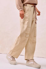 Person wearing beige striped pants and a beige sweater on a plain background