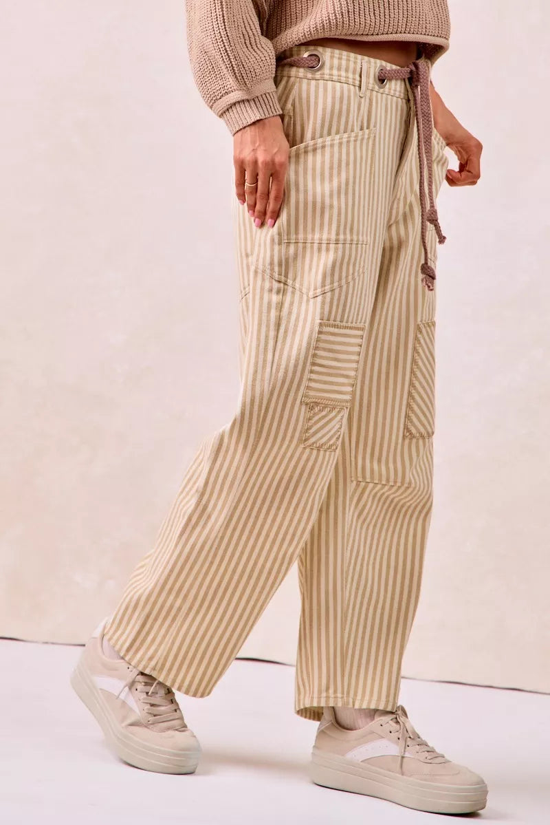 Person wearing beige striped pants and a beige sweater on a plain background