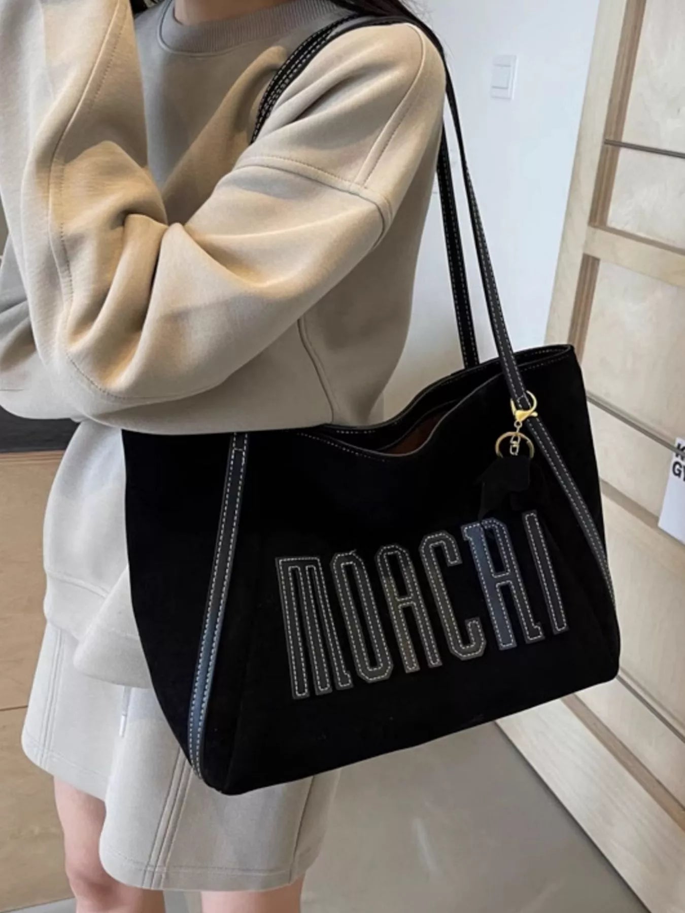 Person holding a black handbag with 'MOACRI' branding.