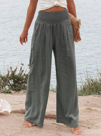 Person wearing wide-leg gray pants standing on a sandy beach with a light blue wall in the background.