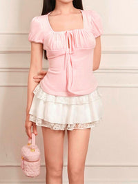 Woman wearing a pink top and white lace skirt holding a matching handbag against a light background