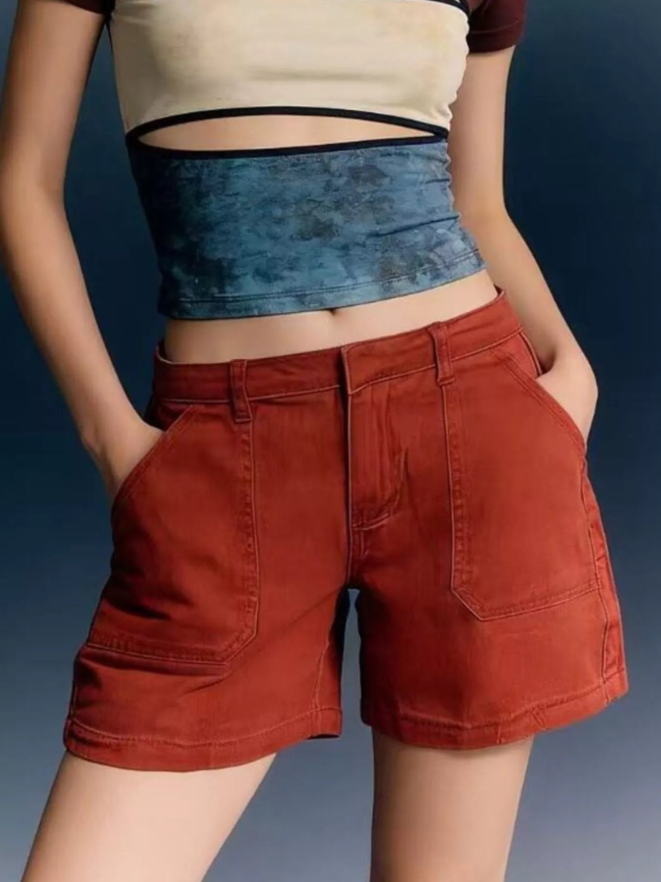 Person wearing a beige crop top and red shorts with a blue denim waistband against a dark background