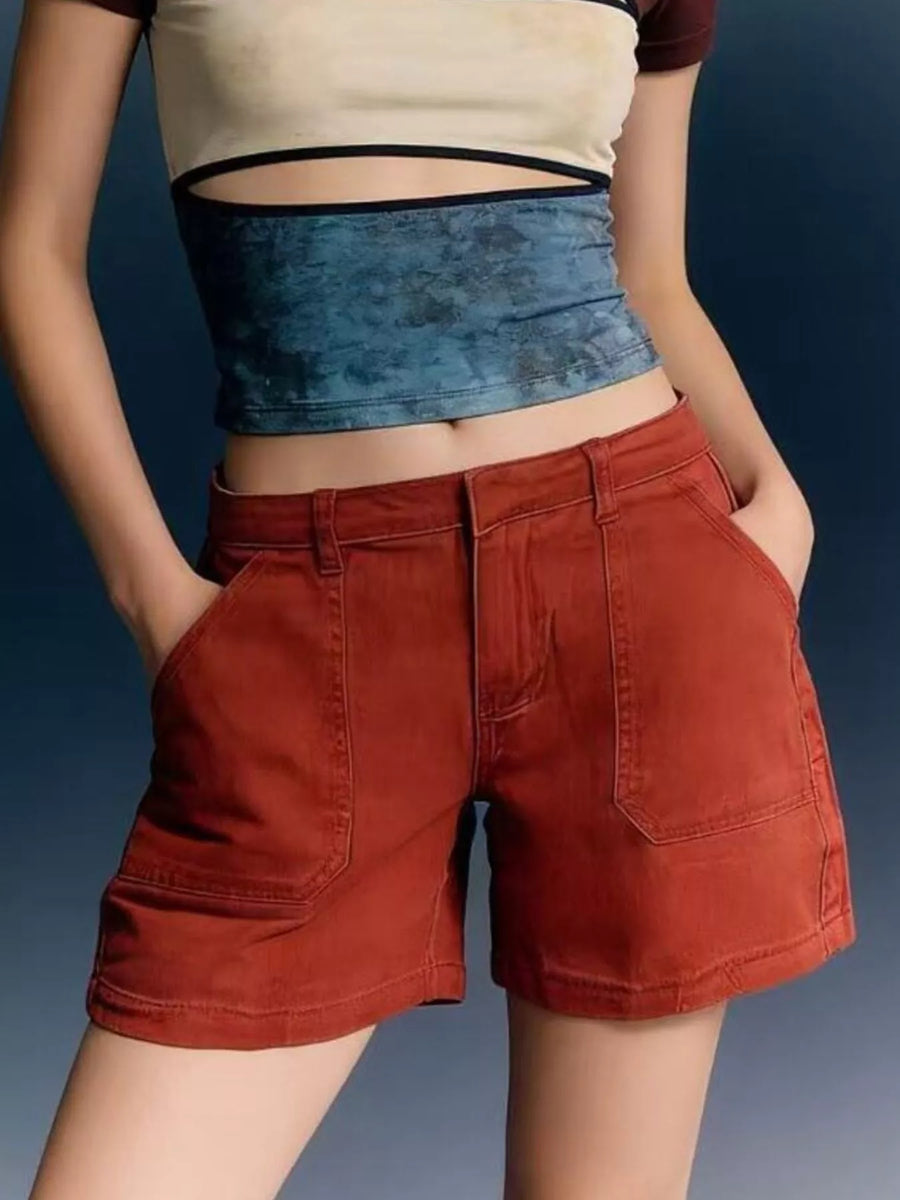 Person wearing a beige crop top and red shorts with a blue denim waistband against a dark background