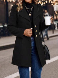Person wearing a black coat with gold buttons, holding a coffee cup on a street.