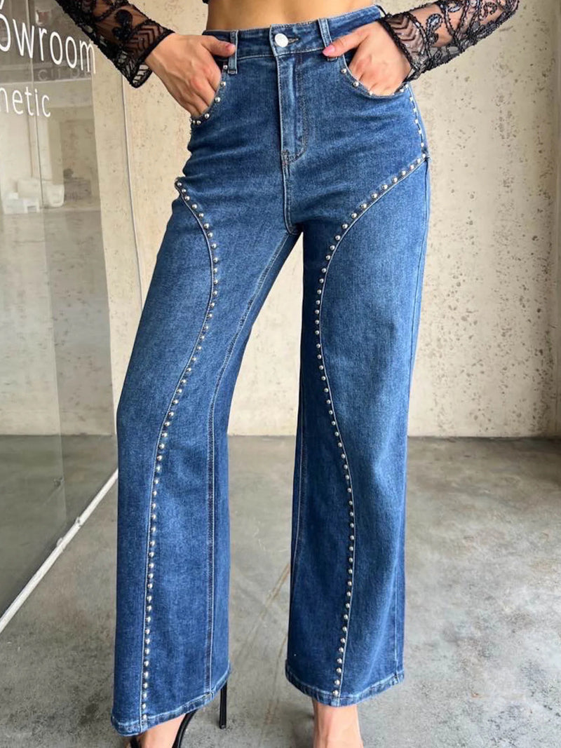 Person wearing high-waisted blue jeans with decorative stitching in an indoor setting.