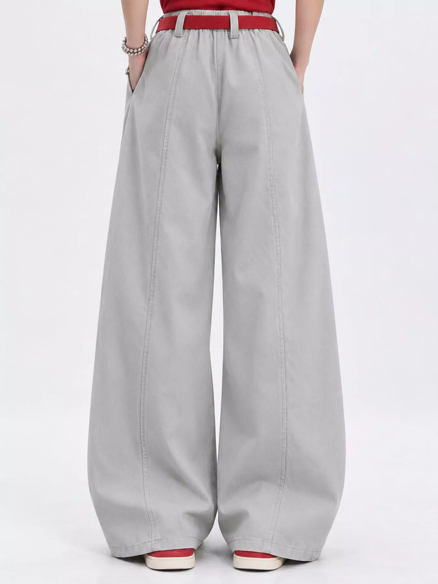 A person shown from the waist down wearing light gray wide-leg trousers with a red belt, a red top, and red-and-white shoes against a plain white studio background.