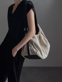 Person wearing a black outfit holding a beige bag against a gray background