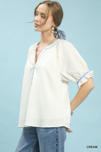 Woman wearing a cream-colored blouse with blue trim against a light blue background