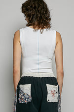 Person wearing a white sleeveless top and black pants with floral pockets on a gray background