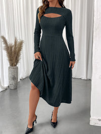 Woman wearing a dark green ribbed dress with long sleeves in a minimalistic setting.