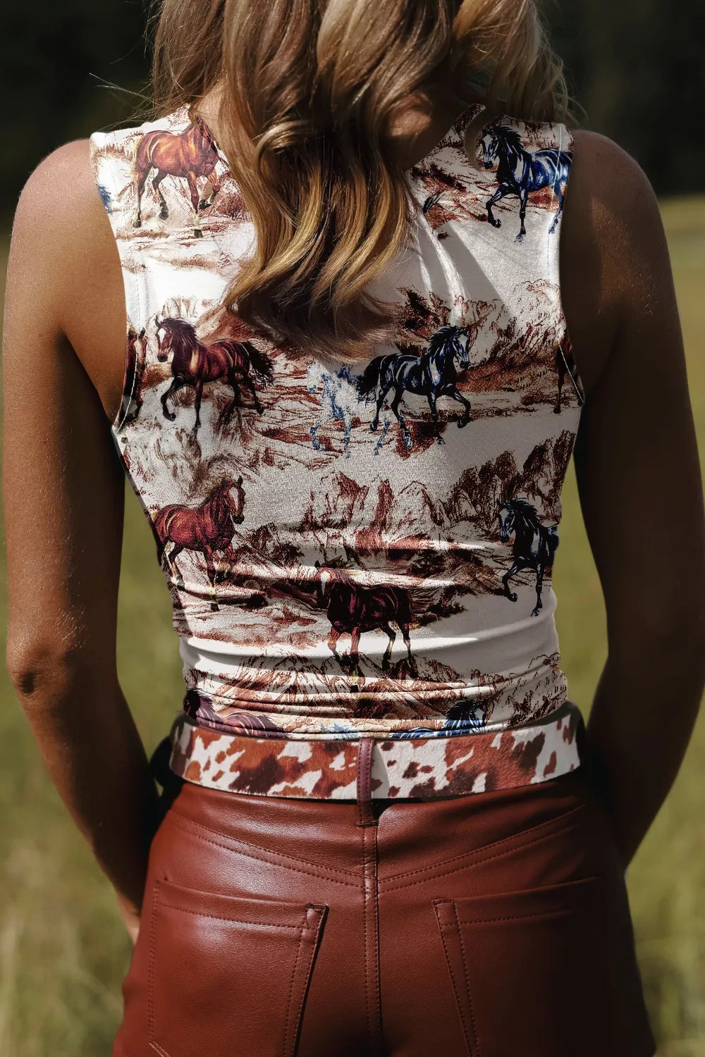 Person wearing a sleeveless top with horse print and brown leather pants in an outdoor setting