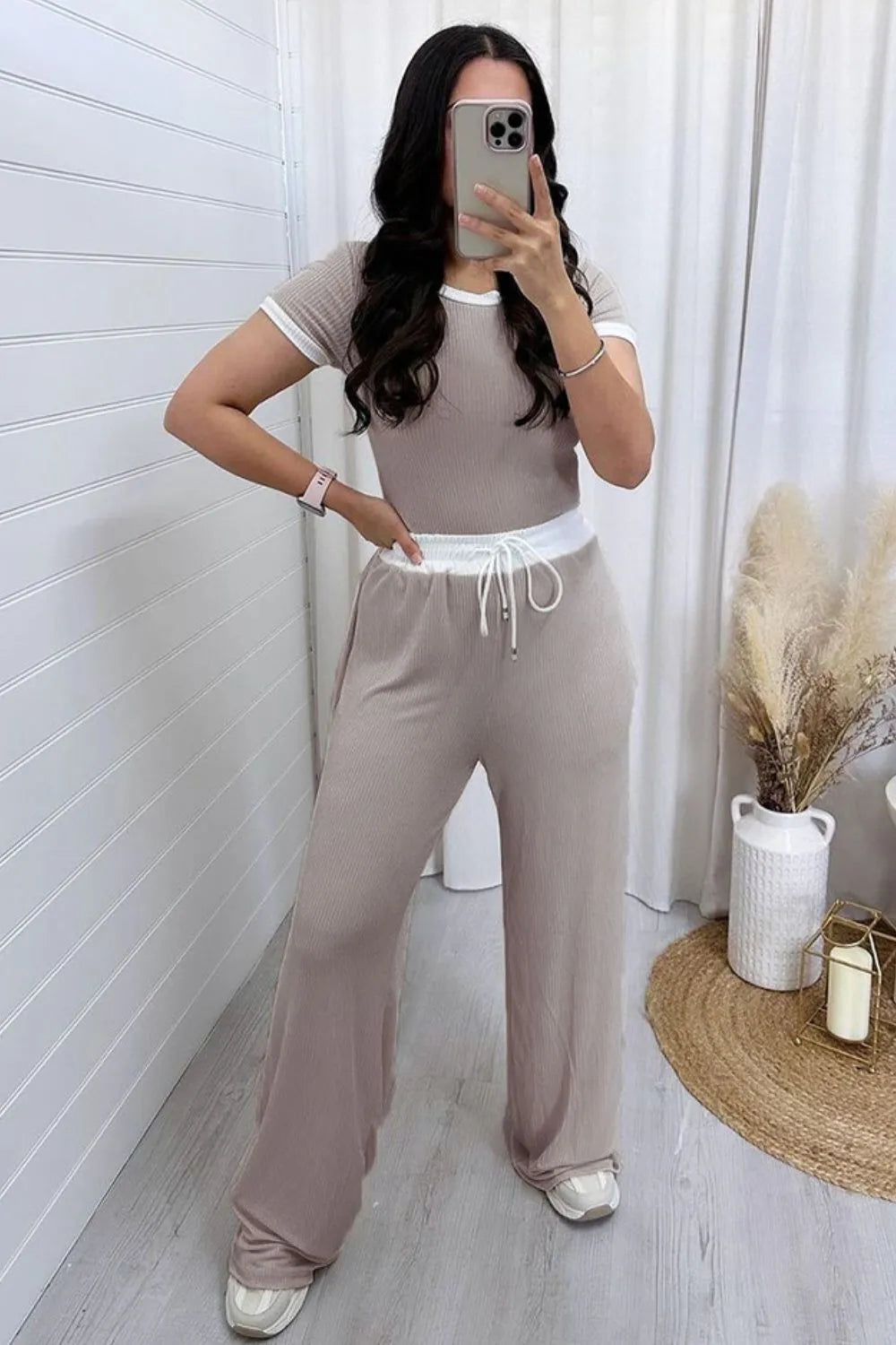 Woman taking a mirror selfie wearing a beige outfit with a white belt.