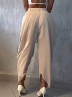 Person wearing beige high-waisted pants and white shoes against a light gray wall.