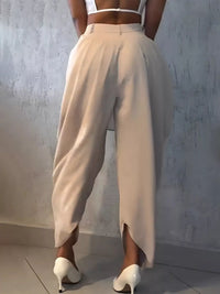 Person wearing beige high-waisted pants and white shoes against a light gray wall.