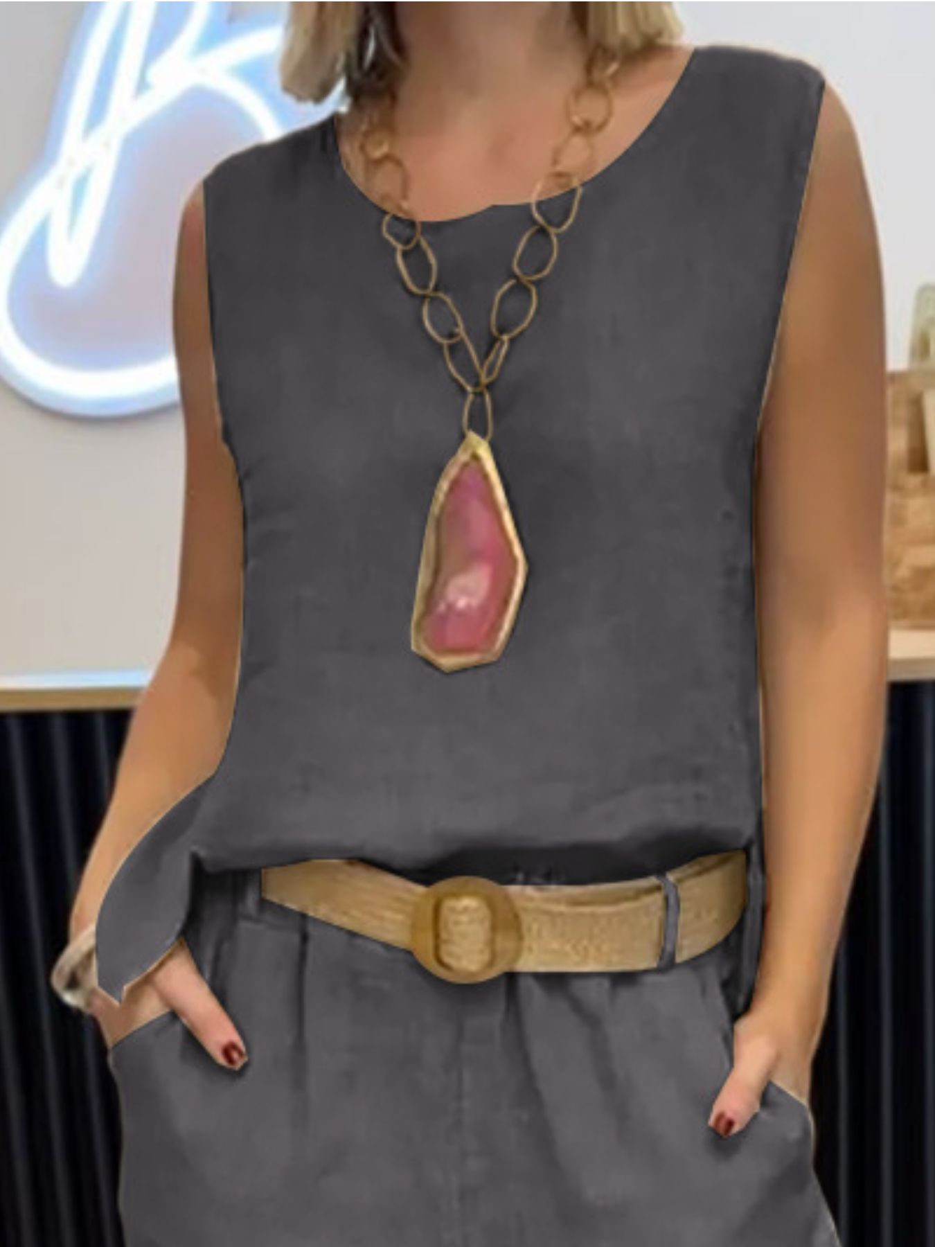 Person wearing a gray sleeveless top with a large necklace and belt, standing indoors.