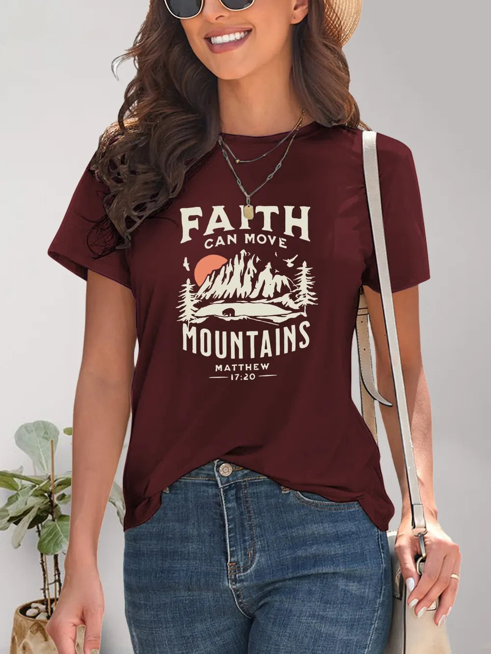 Woman wearing a maroon t-shirt with 'Faith Can Move Mountains' graphic and text.