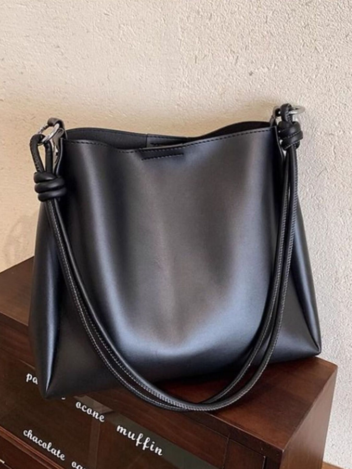 Black leather handbag on a wooden surface with a neutral background