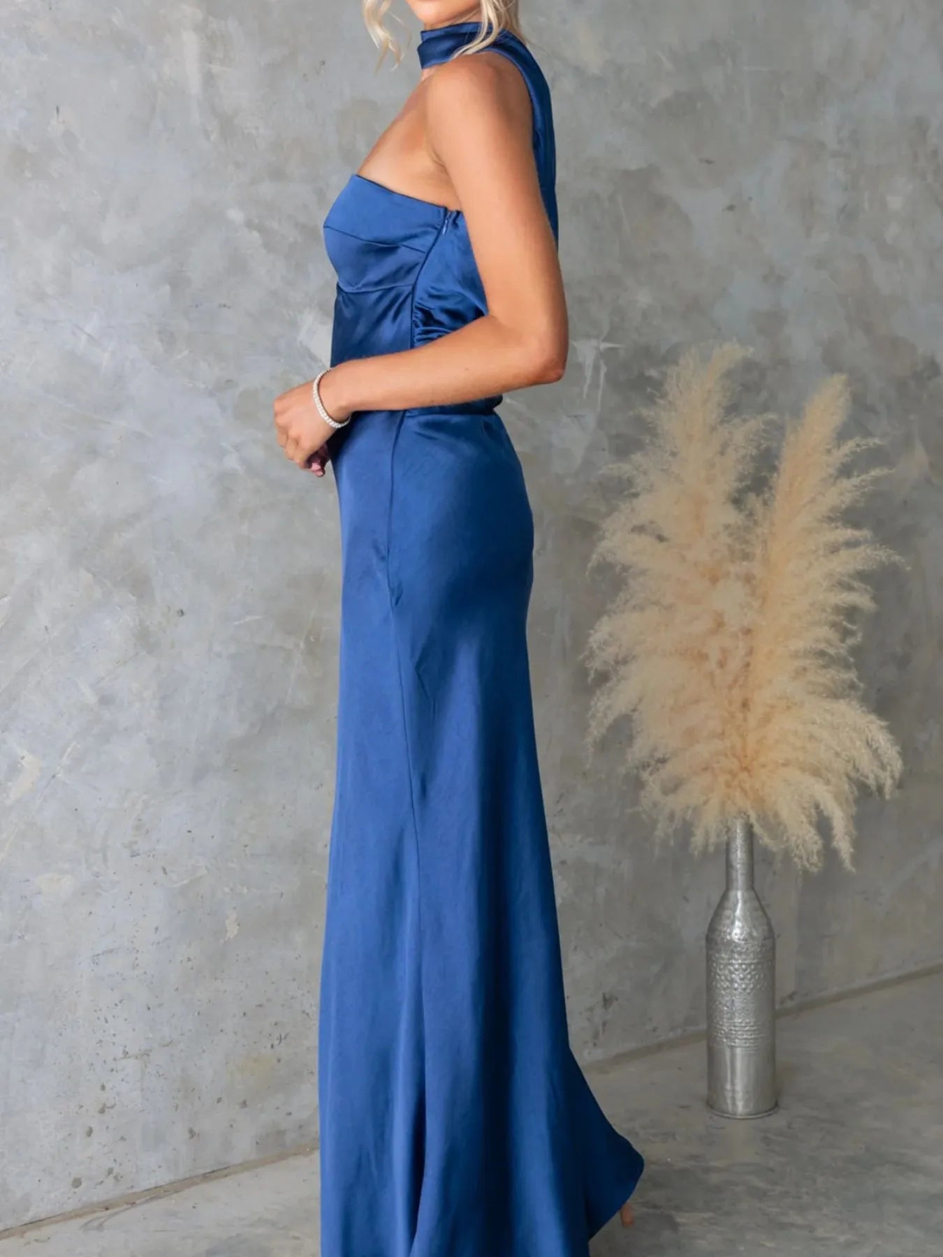 Woman wearing a blue evening gown against a gray wall with decorative elements.