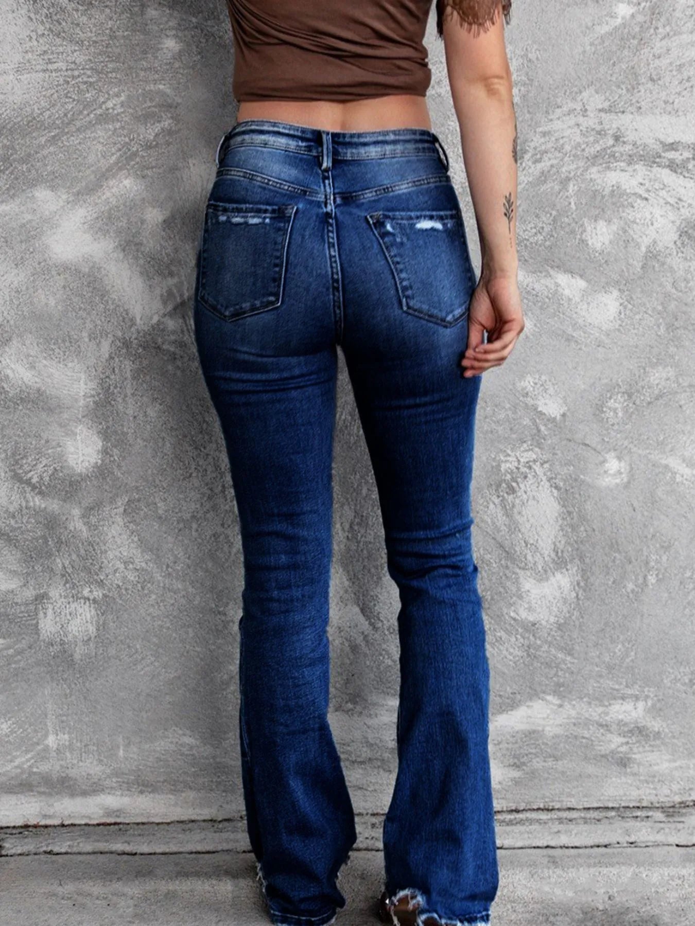 Person wearing blue flared jeans against a textured gray wall.