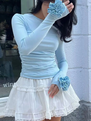 Person wearing a light blue long-sleeve top and white skirt with decorative gloves.