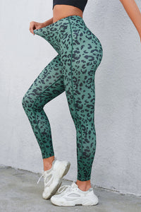 Green leopard print leggings worn by a person against a white wall.