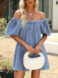 Woman wearing a blue off-shoulder dress holding a white clutch outdoors.