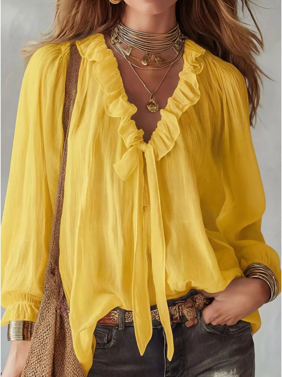 Yellow blouse with ruffled details worn by a person, on a neutral background