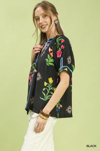 Woman wearing a black floral embroidered top against a light green background