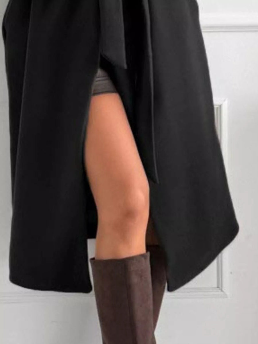 Person wearing a black coat and brown knee-high boots against a white wall.