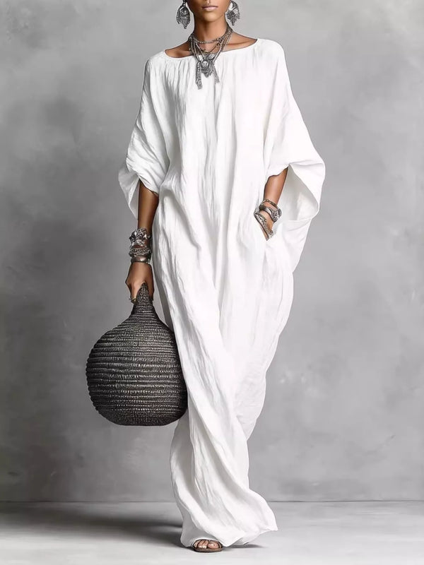 Woman in a long white dress holding a textured black handbag against a gray background