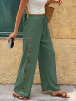 Green pants with floral cutouts worn by a person against a beige wall.