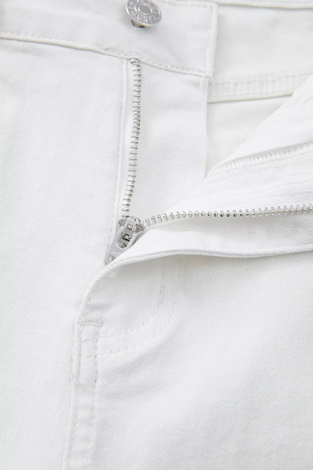 Close-up of a white denim zipper and button on a white background