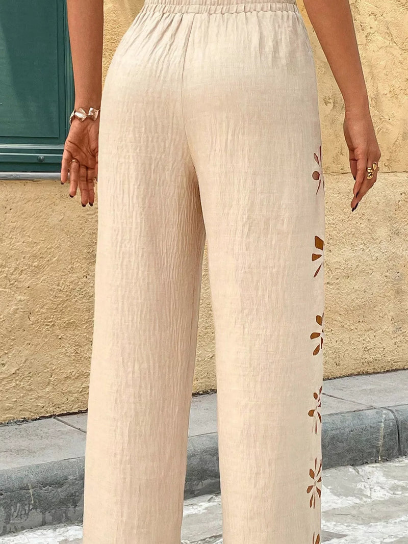 Beige pants with floral patterns on a person standing against a beige wall.