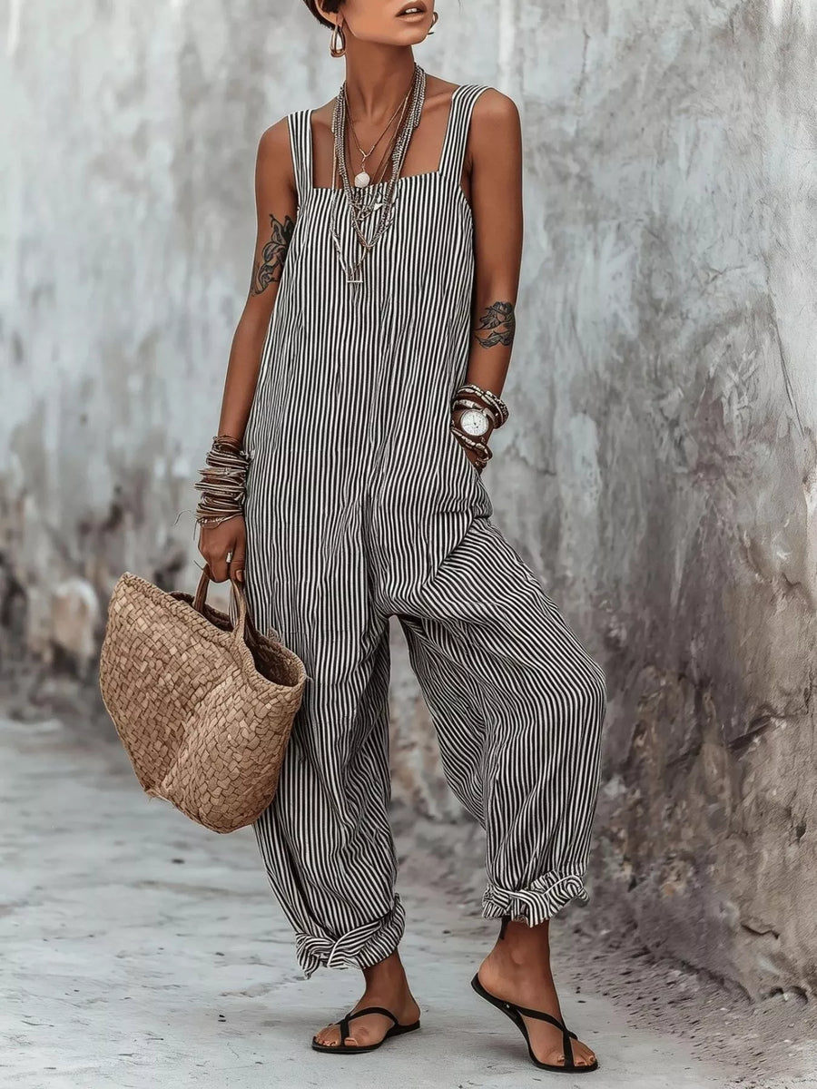 Person wearing a striped jumpsuit holding a woven bag against a textured wall.