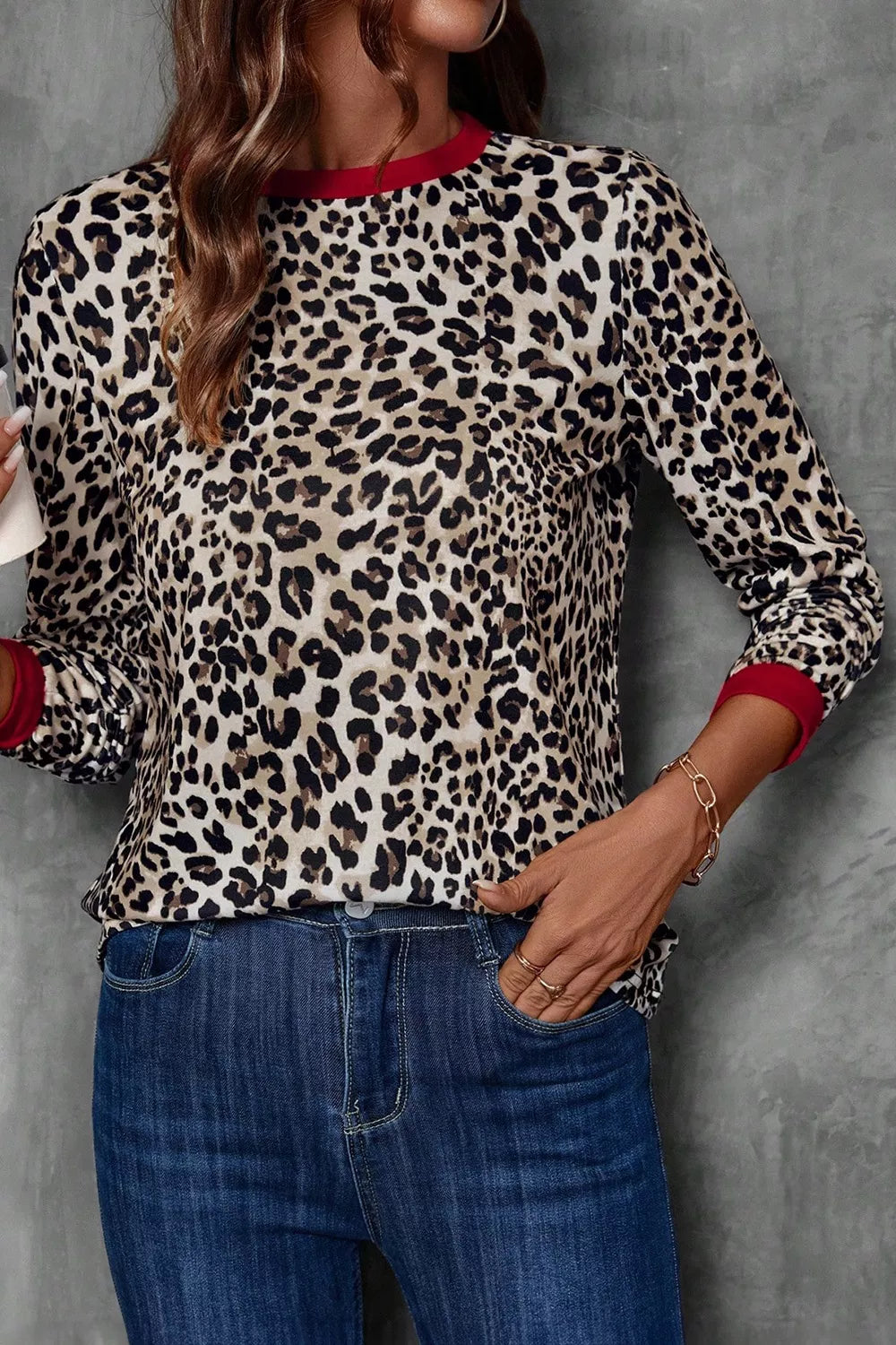 Person wearing a leopard print top with red cuffs and trim, paired with blue jeans against a gray background.