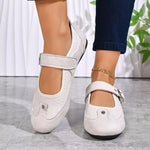 A pair of women's Mary Jane style shoes in off-white textured faux leather, shown on a model's feet. The shoes feature a single hook-and-loop strap with a silver metal snap closure and a decorative stud on the toe.