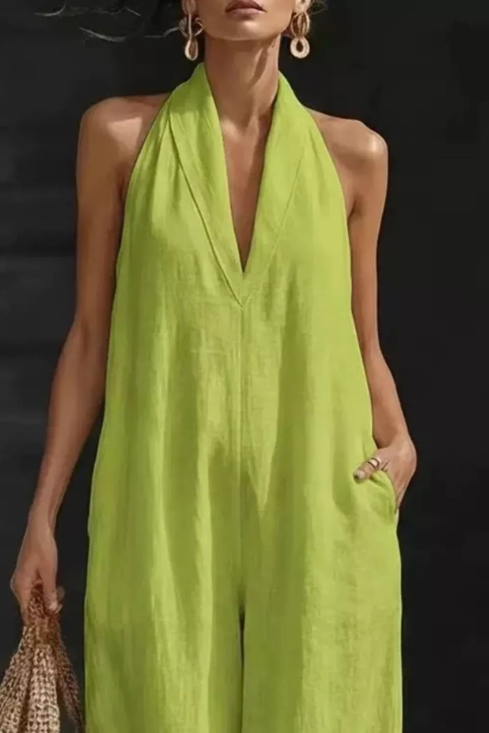 Woman wearing a bright green halter neck jumpsuit against a black background