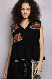 Woman wearing a black sleeveless top with floral embroidery against a gray background
