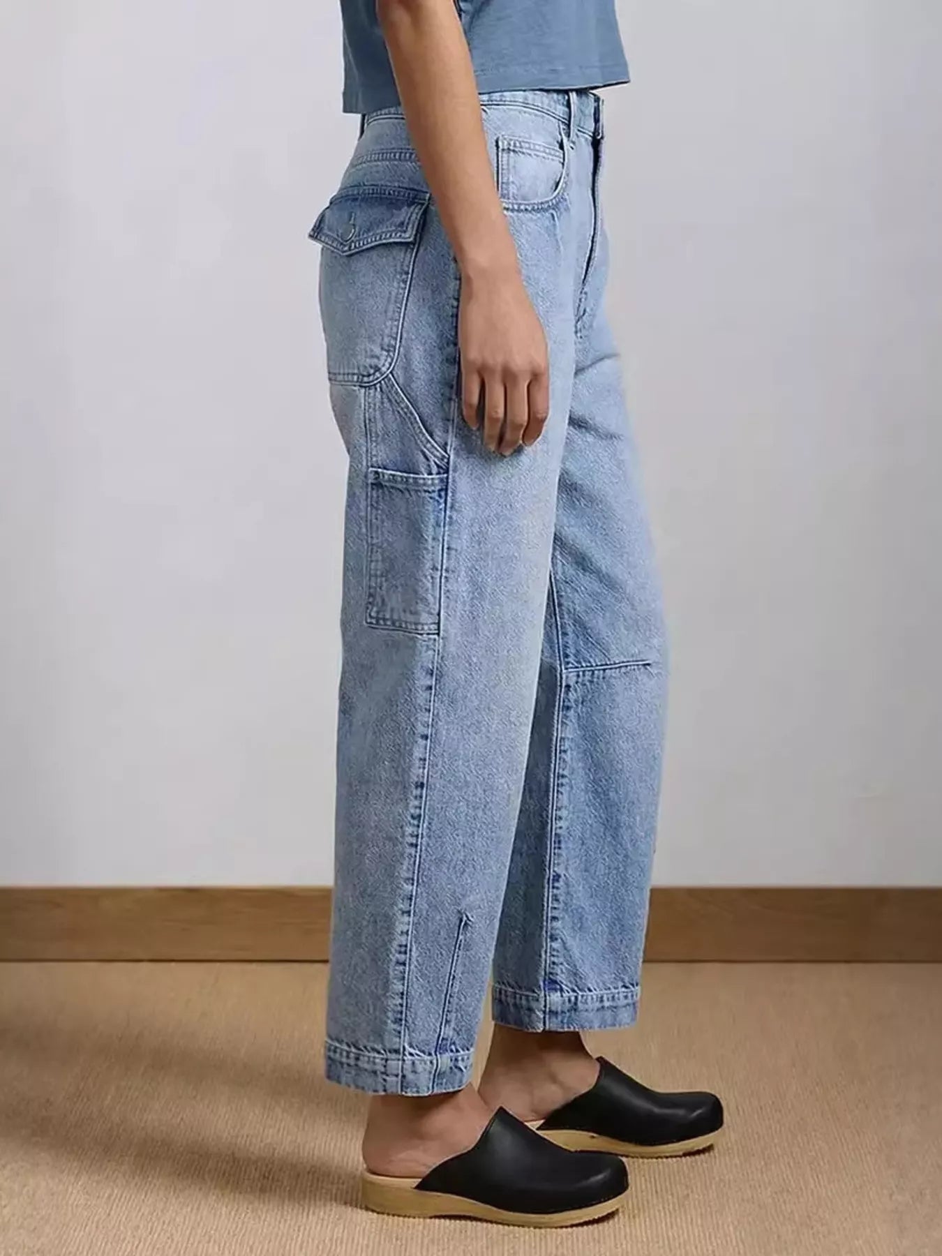 Person wearing light blue jeans and black clogs on a neutral background