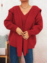 Person wearing a red hooded sweater against a white brick wall.