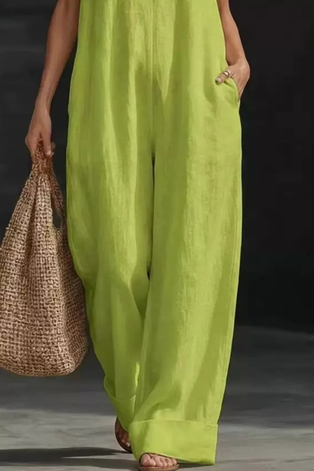 Person wearing bright green pants holding a woven bag against a dark background