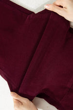 A close-up of a pair of burgundy corduroy shorts being held by hands to show the texture and fit.