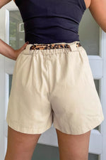 Person wearing beige shorts with a leopard print belt and navy top.