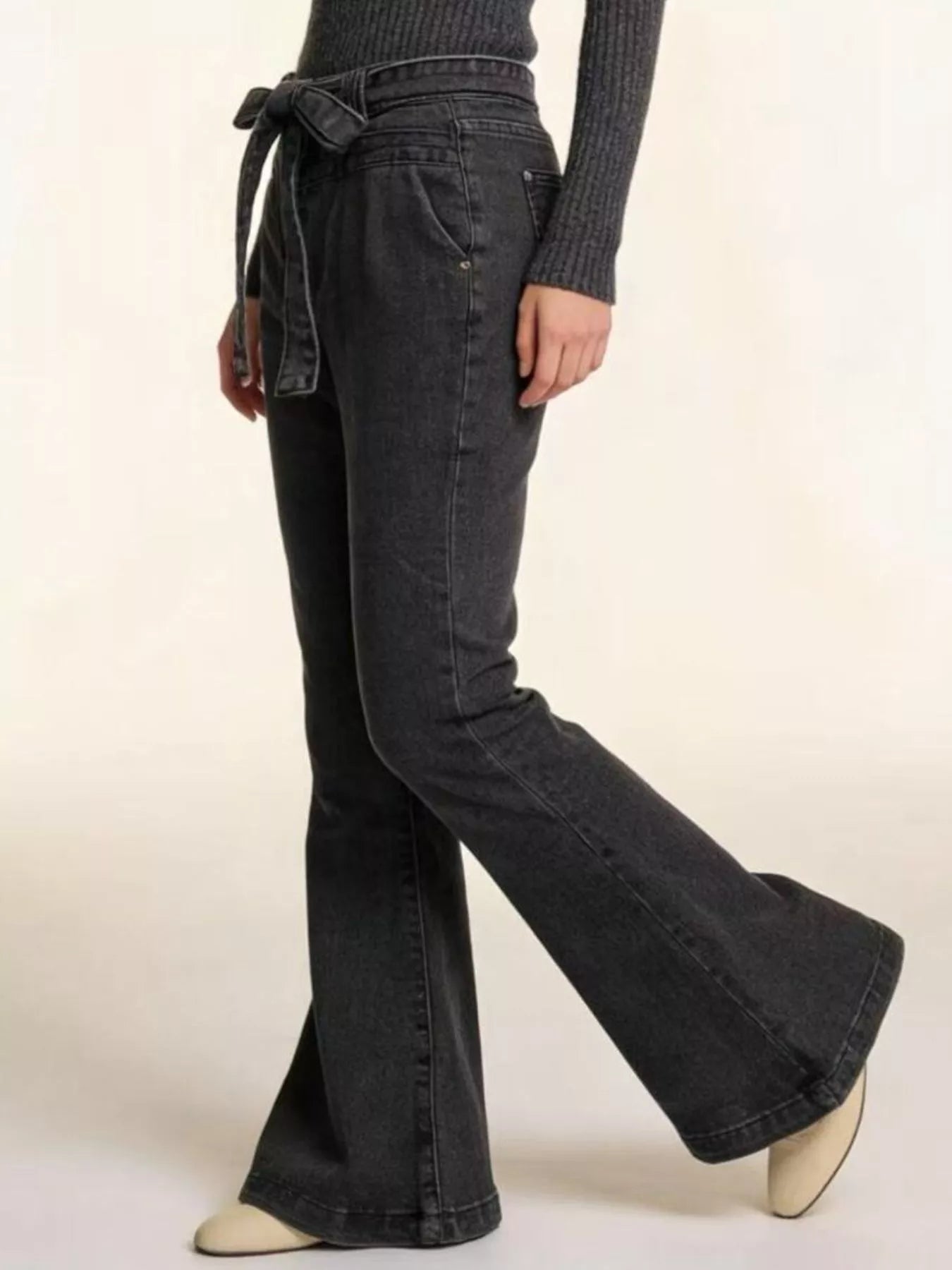 Person wearing black flared jeans on a plain background