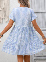 Woman wearing a blue and white checkered dress against a wooden wall.