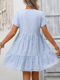 Woman wearing a blue and white checkered dress against a wooden wall.