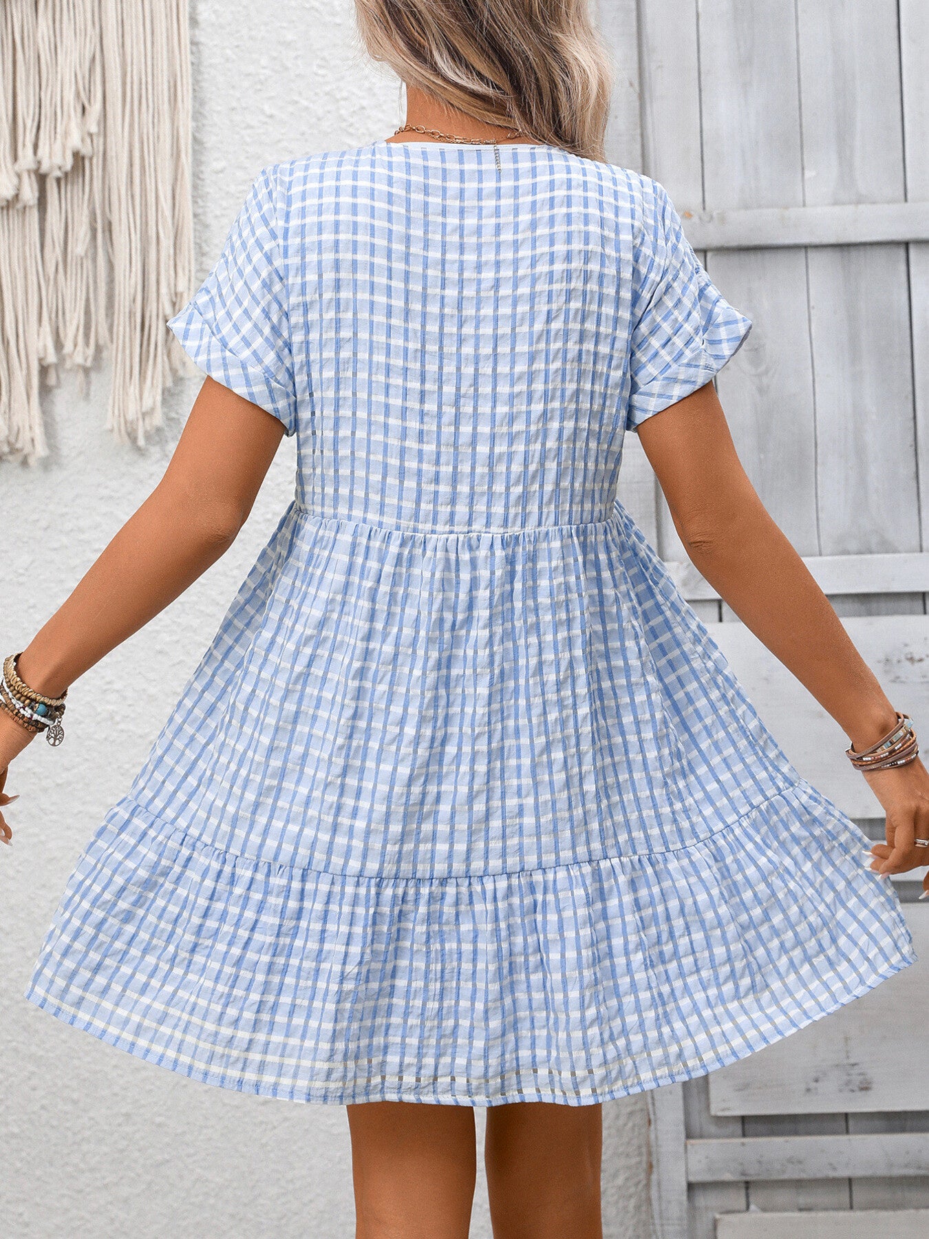 Woman wearing a blue and white checkered dress against a wooden wall.