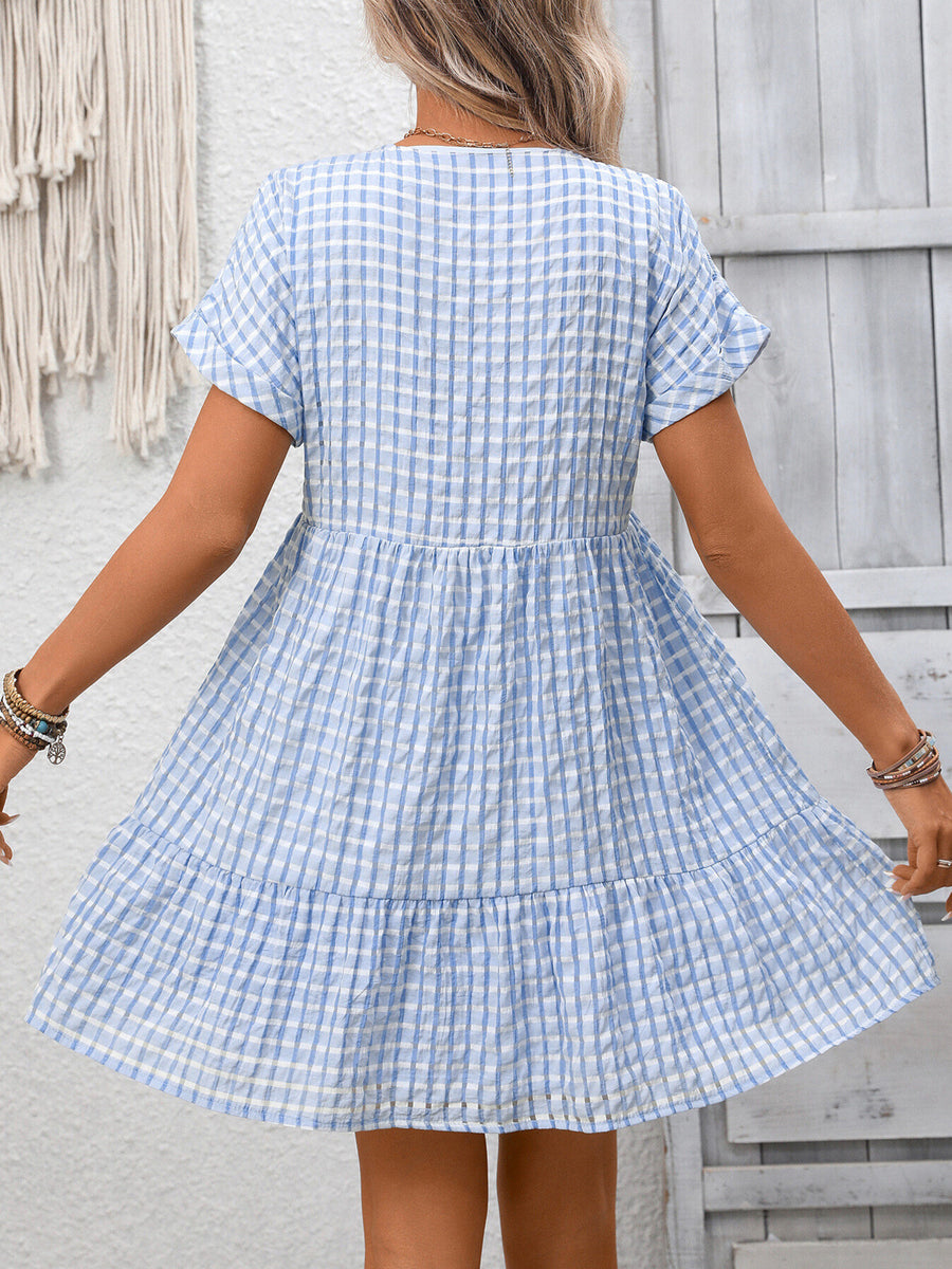 Woman wearing a blue and white checkered dress against a wooden wall.