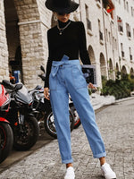 Person wearing a black top and blue jeans standing on a street with motorcycles in the background